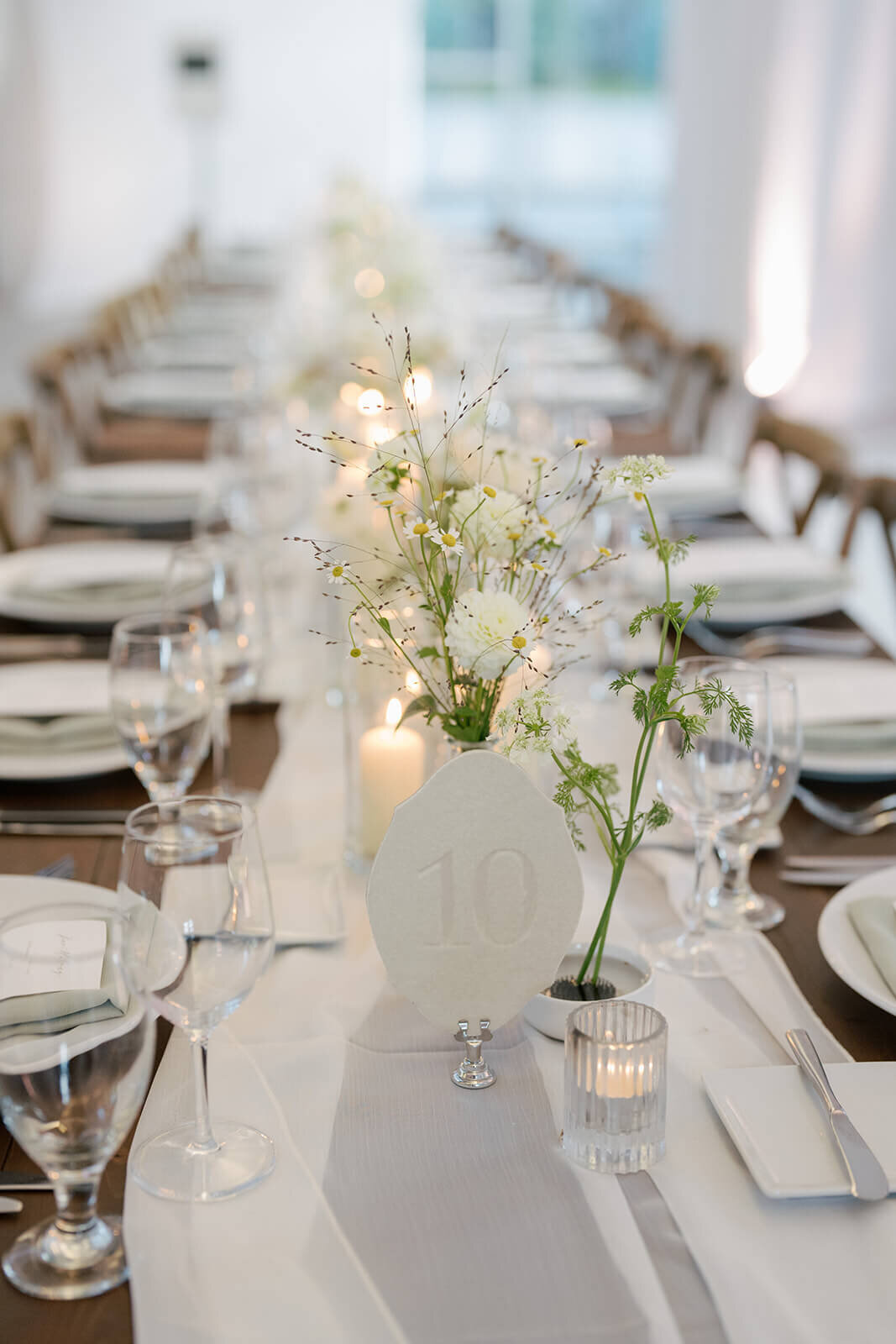 A long dinner table adorned with simple white seasonal Colorado wildflowers and candle votives at the Aspen Meadows Resort wedding reception.