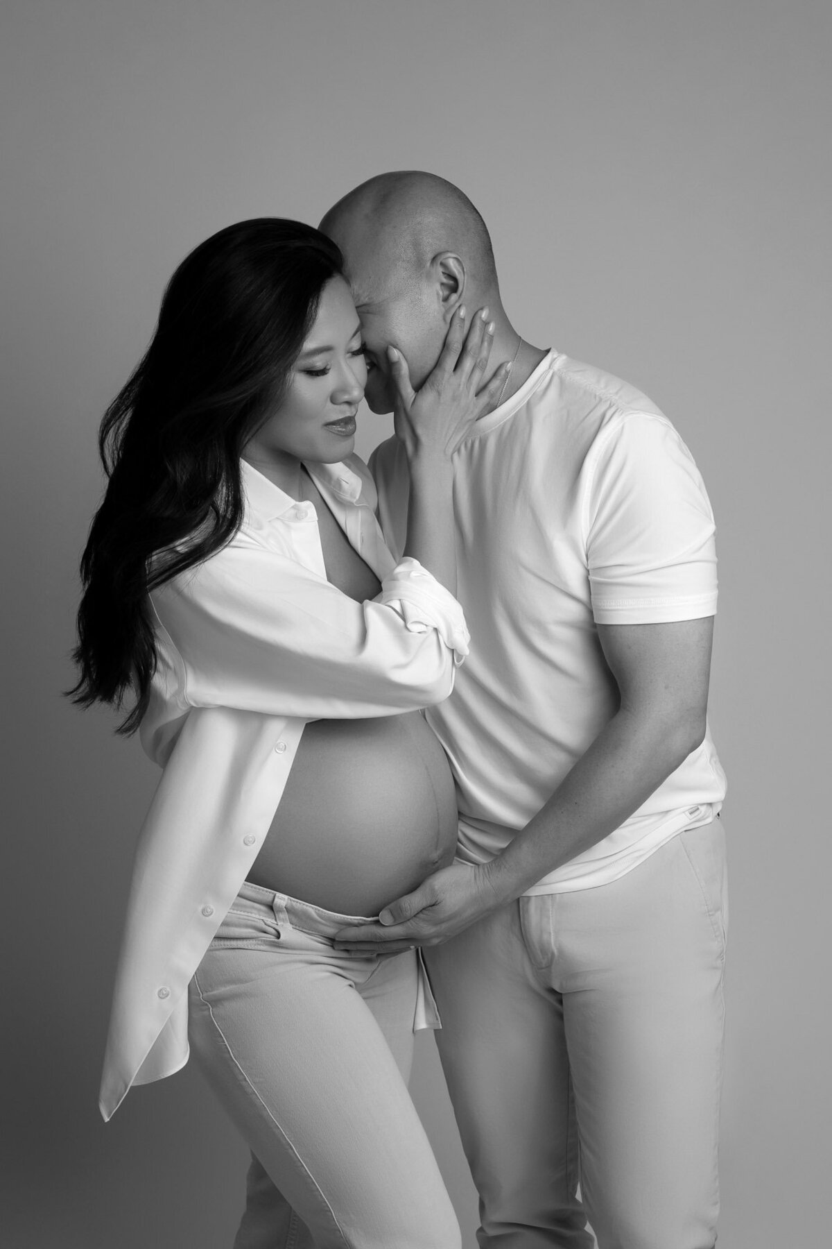 Intimate maternity photo of pregnant woman in white dress sitting pose during studio session