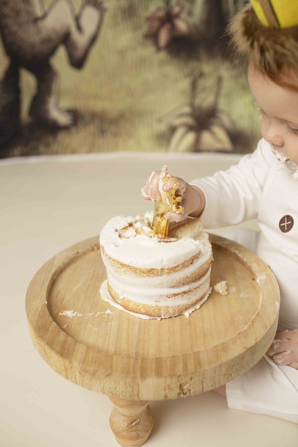 One-year-old redhead birthday boy with a crown on his head, joyfully smashing his Where the Wild Things Are themed birthday cake