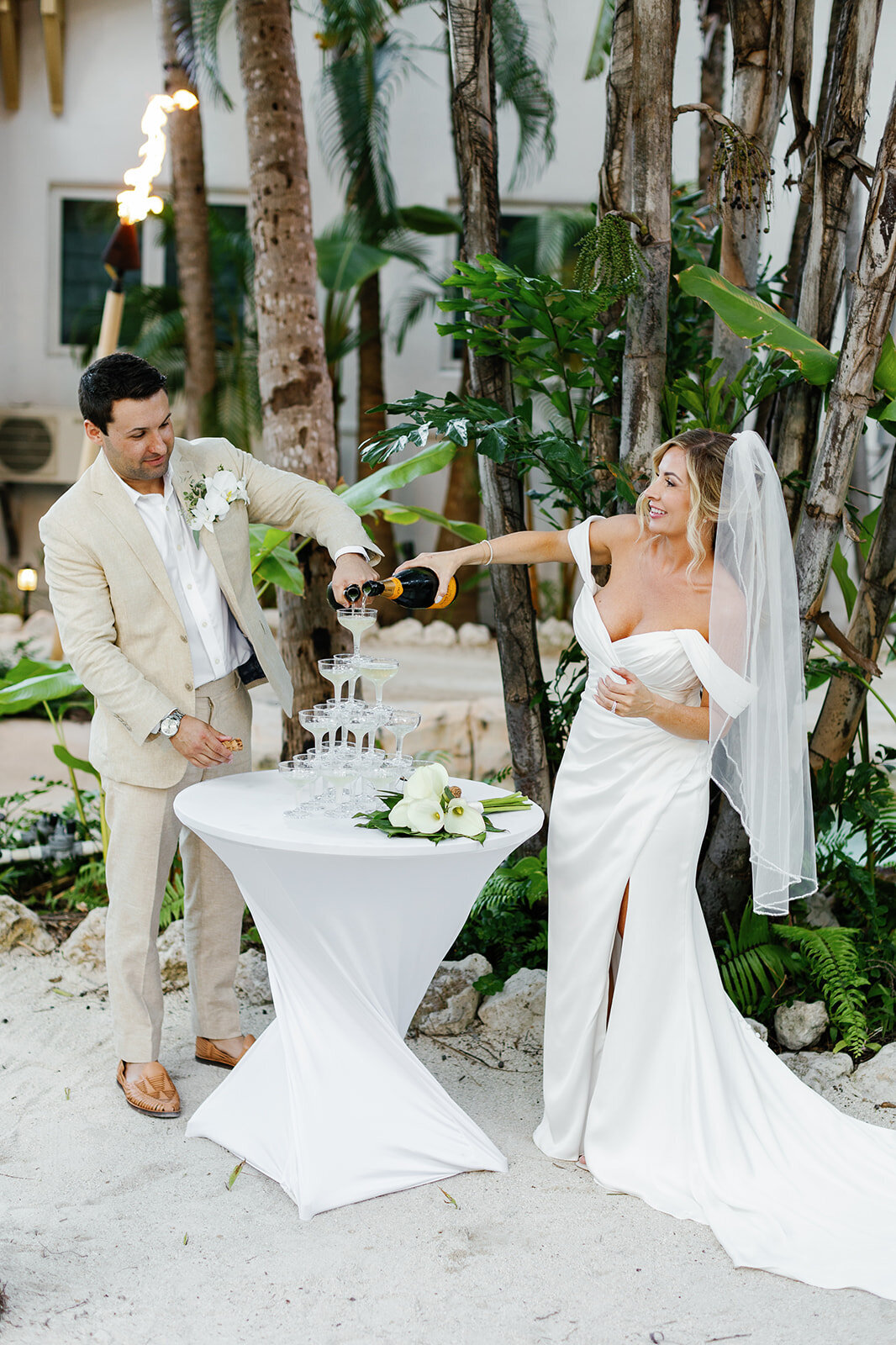 The couple pours champagne into a stunning tower, a fun addition to their elegant Florida Keys reception.