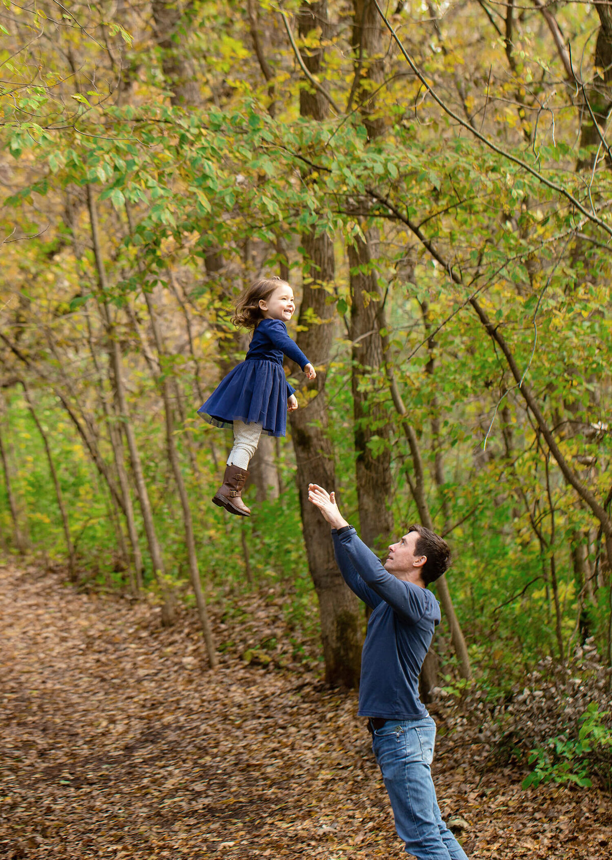 Dad throwing toddler girl really high in the air in the woods.