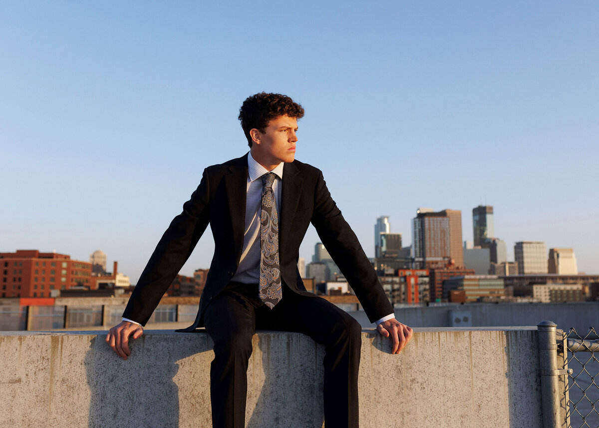 Senior Guy posing on parking ramp in well-fitting suit in front of minneapolis skyline