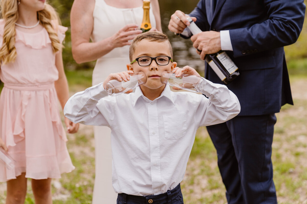 Son of groom presses to glasses to his cheeks during his parents elopement at Officers Gulch Pond, Colorado