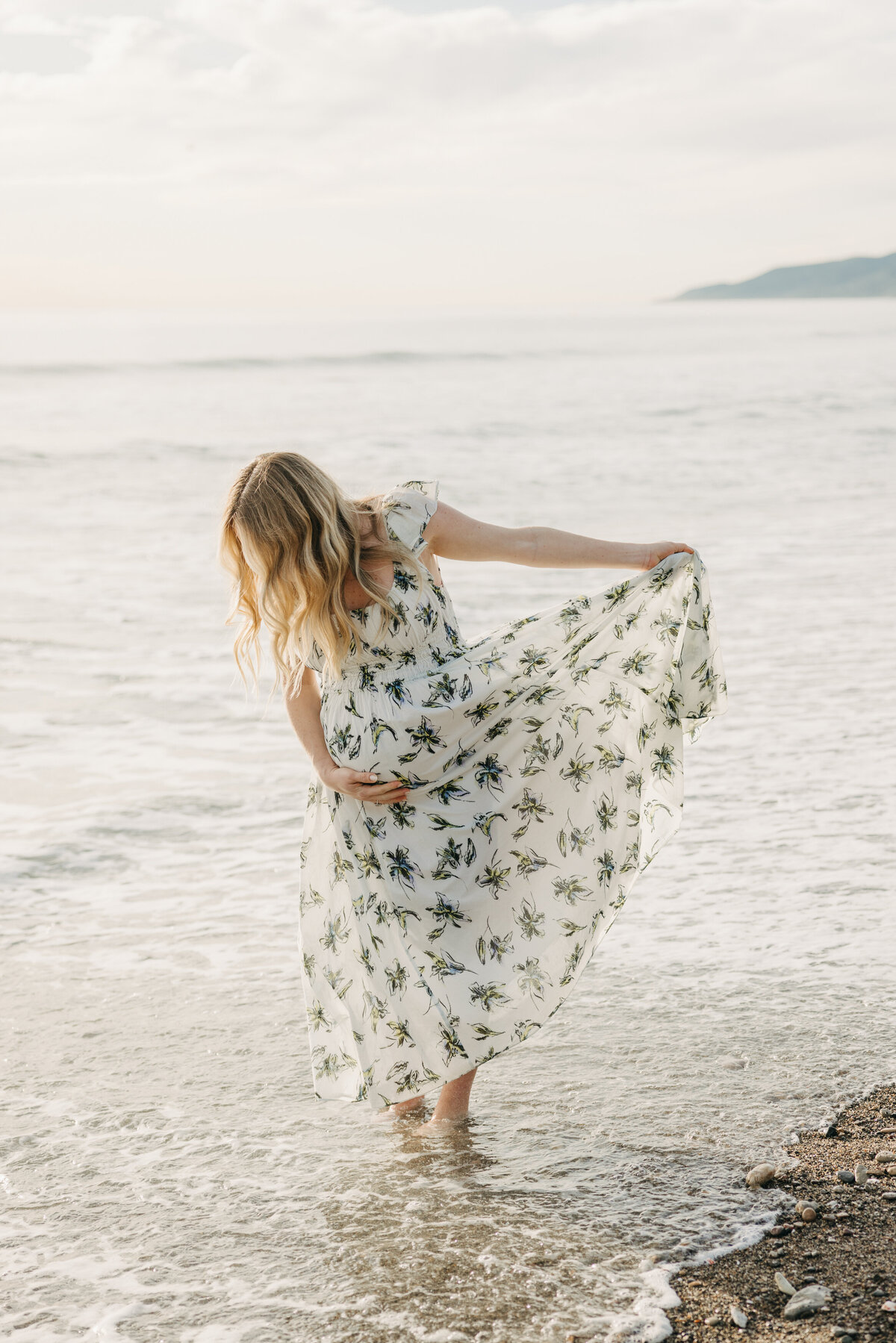 Maternity session holding dress on the beach as the tide comes in over her toes.