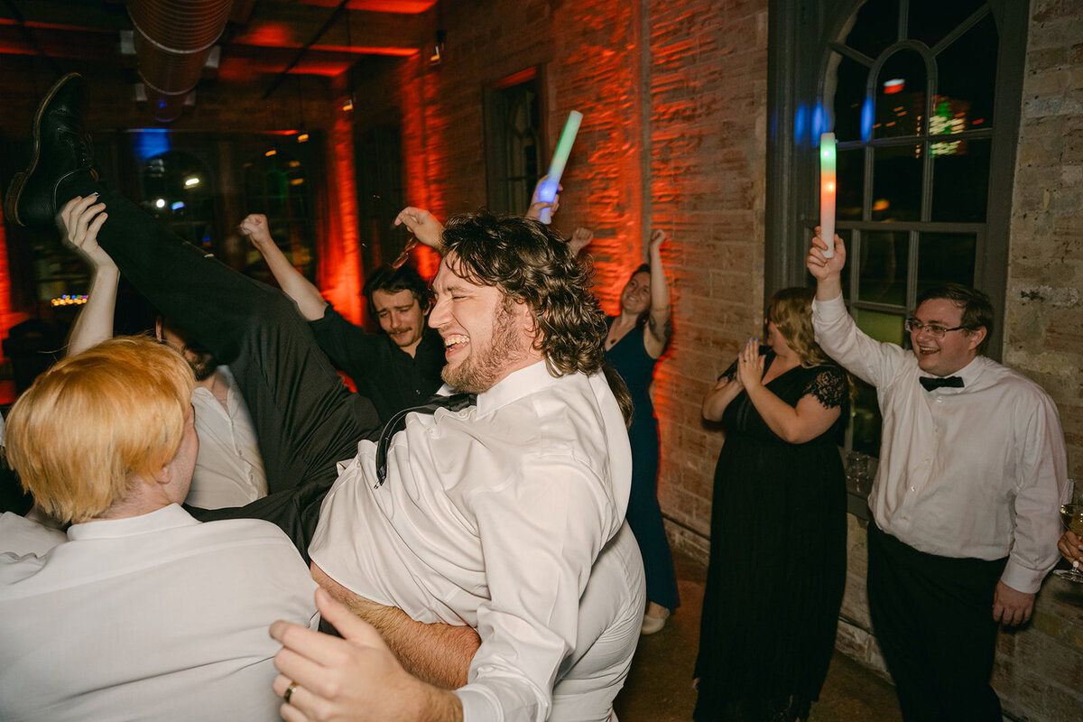 Groom laughing while being lifted into the air by guests during high-end San Antonio wedding reception at The Battalion