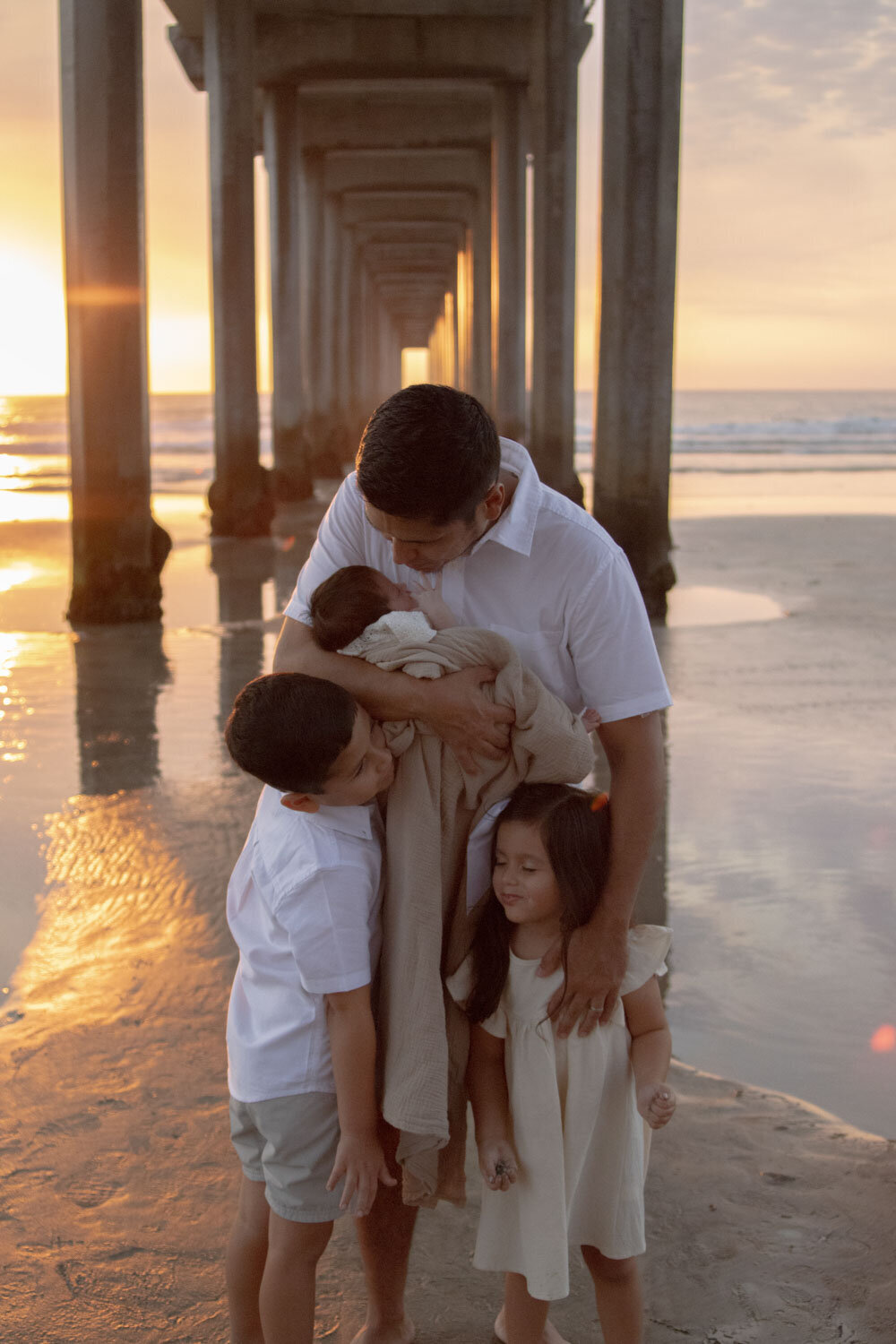 Father embracing his three children under a pier at sunset