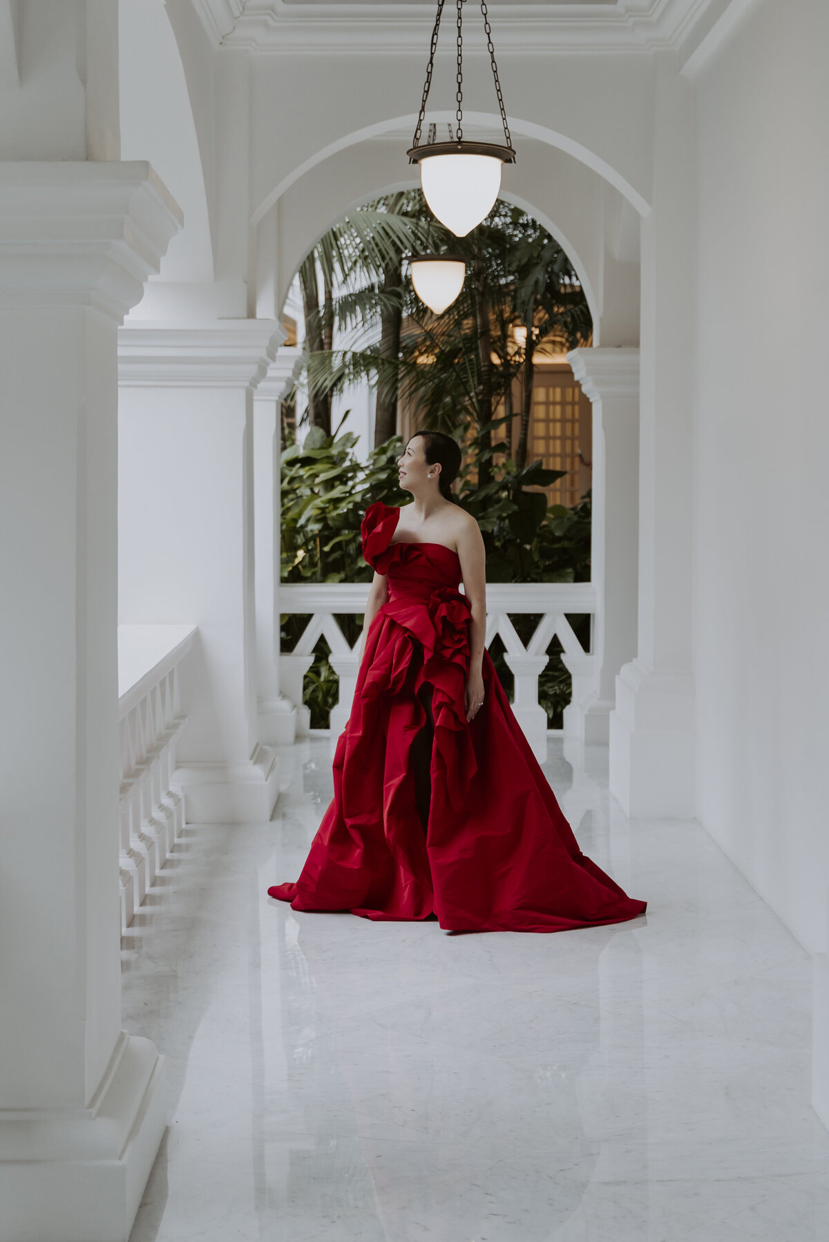 a woman in a read cheongsam dress looks up at the raffles hotel view