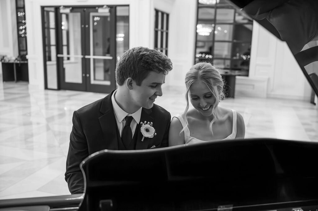 black and white image of wedding couple sitting at a piano together