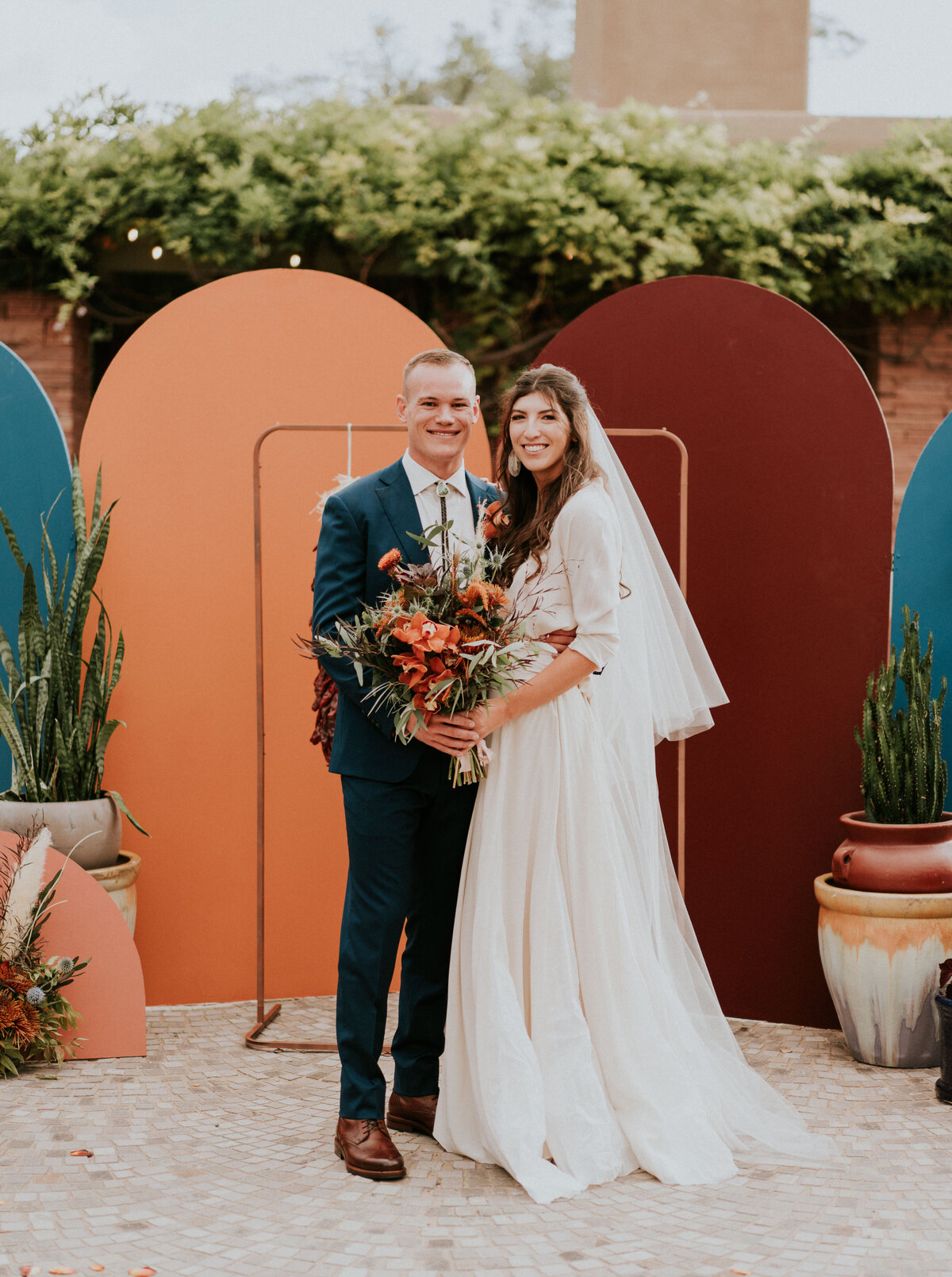 Bride and groom pose for a photo in front of their wedding ceremony backdrop.