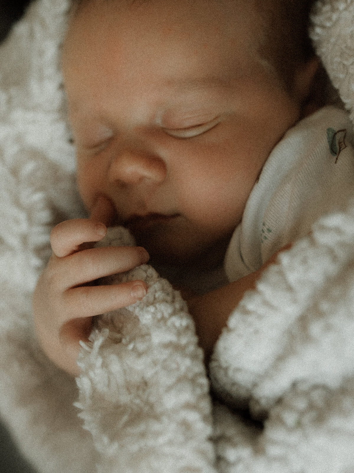 Close-up of a sleeping newborn wrapped in a cozy white blanket, gently holding the edge with tiny fingers.
