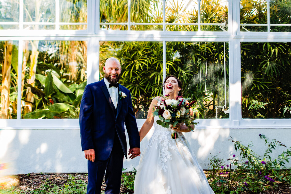 One of the top wedding photos of 2020. Taken by Adore Wedding Photography- Toledo, Ohio Wedding Photographers. This photo is of bride and groom laughing in front of a lush green house at the Zoo