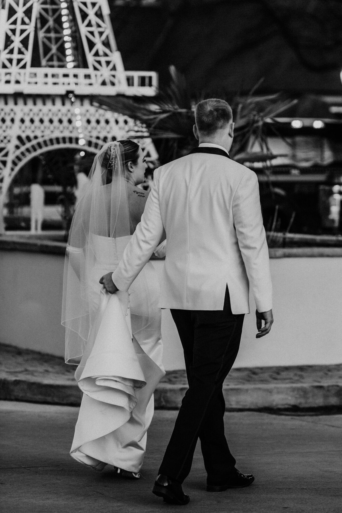 groom w=holds his brides dress as they walk together