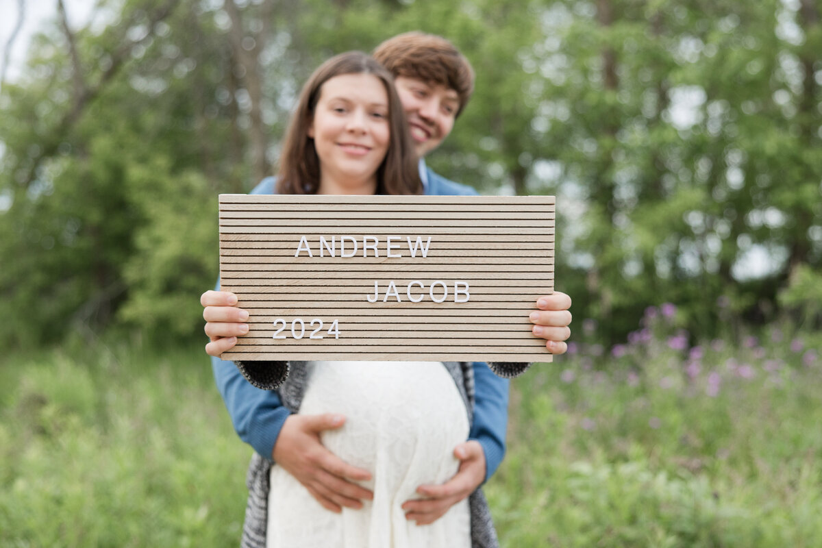 Expectant couple holding each other with the name of the baby on a plaque