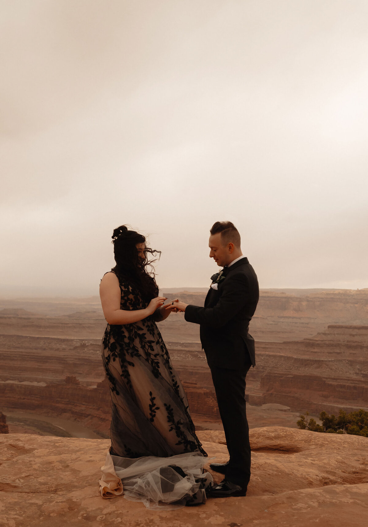 groom puts ring on his bride's finger during their elopement ceremony on a moody day at Dead Horse Point State Park in Moab, Utah