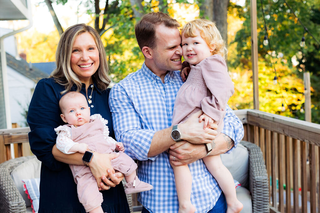 Two parents stand outside on a porch with their two kids.