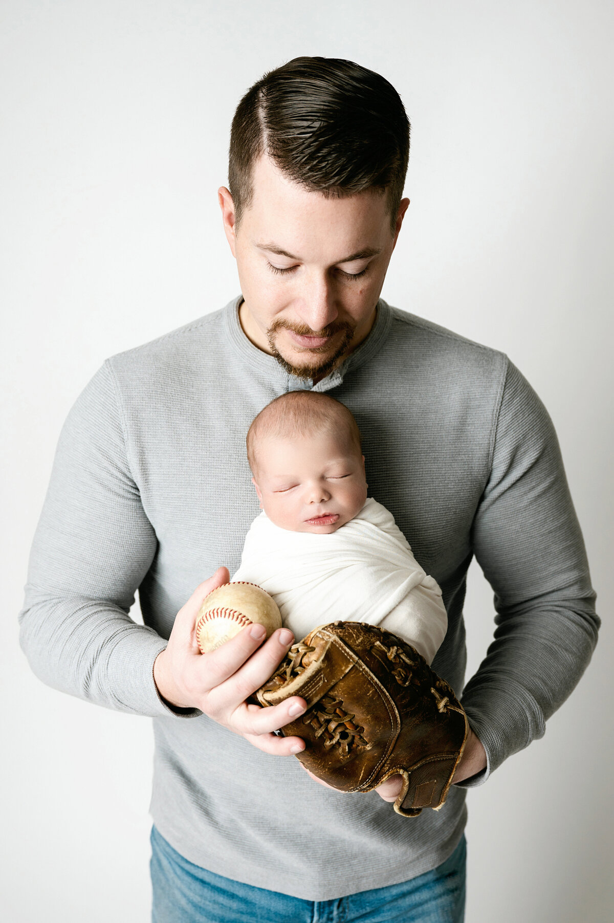 A unique and heartfelt moment between father and baby, captured with a baseball glove and ball in our Pittsburgh newborn photography studio. A perfect tribute to fatherhood.