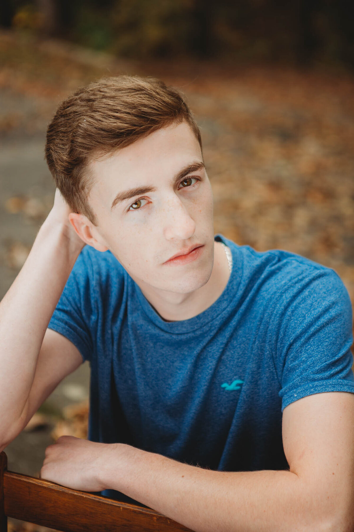 Red headed senior boy sitting backward in a chair wearing a blue shirt.