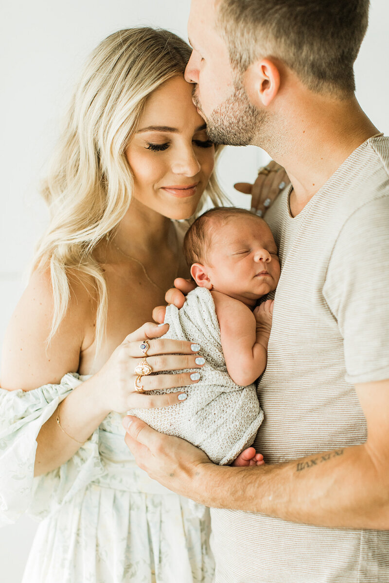 Nashville’s Hunter Premo snuggles newborn as husband kisses her forehead in photographer studio