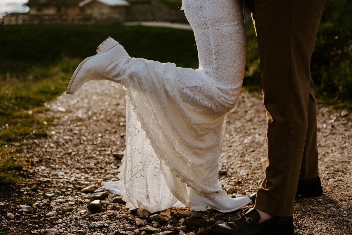 Bride lifting dress hem while walking on rocky trail”