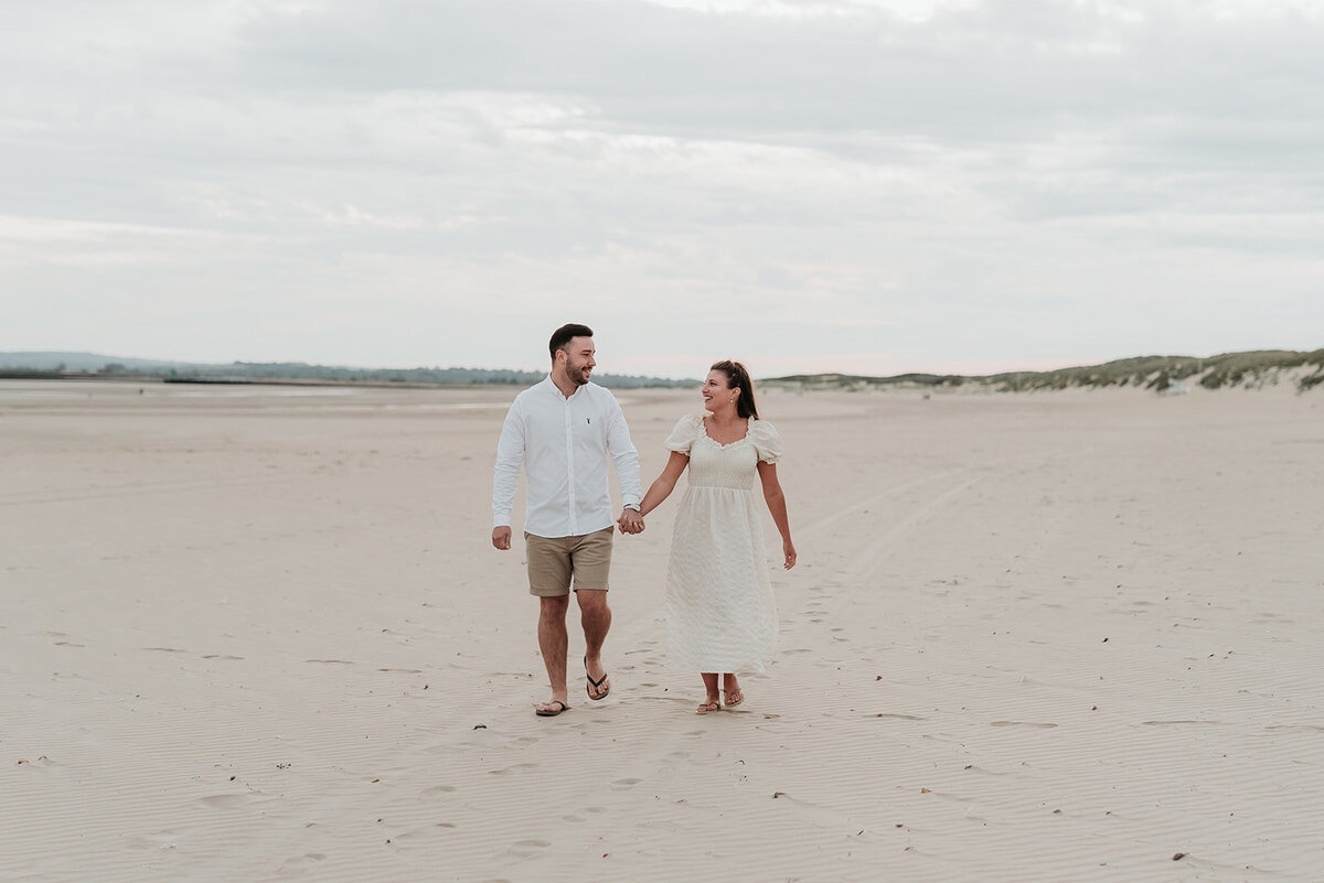 Couple walking and smiling hand in hand along the sandy beach at Camber Sands, Rye