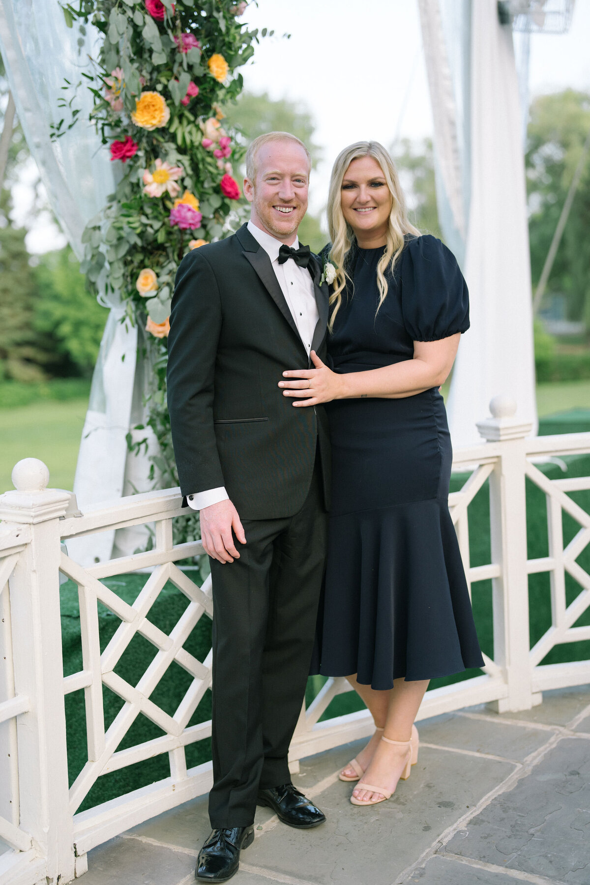 A couple posing by a decorative white gazebo at the wedding venue.