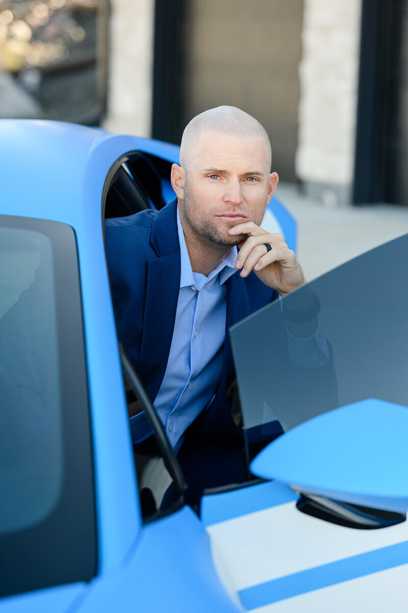 A brand photographer takes a picture of a man in a blue suit sitting in a blue Lamborghini  for his branding photos and brand photography shoot.