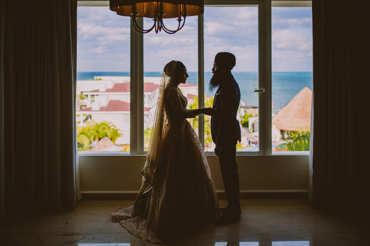 Sikh amritdhari wedding couple stand in front of a window at the moon palace cancun in mexico
