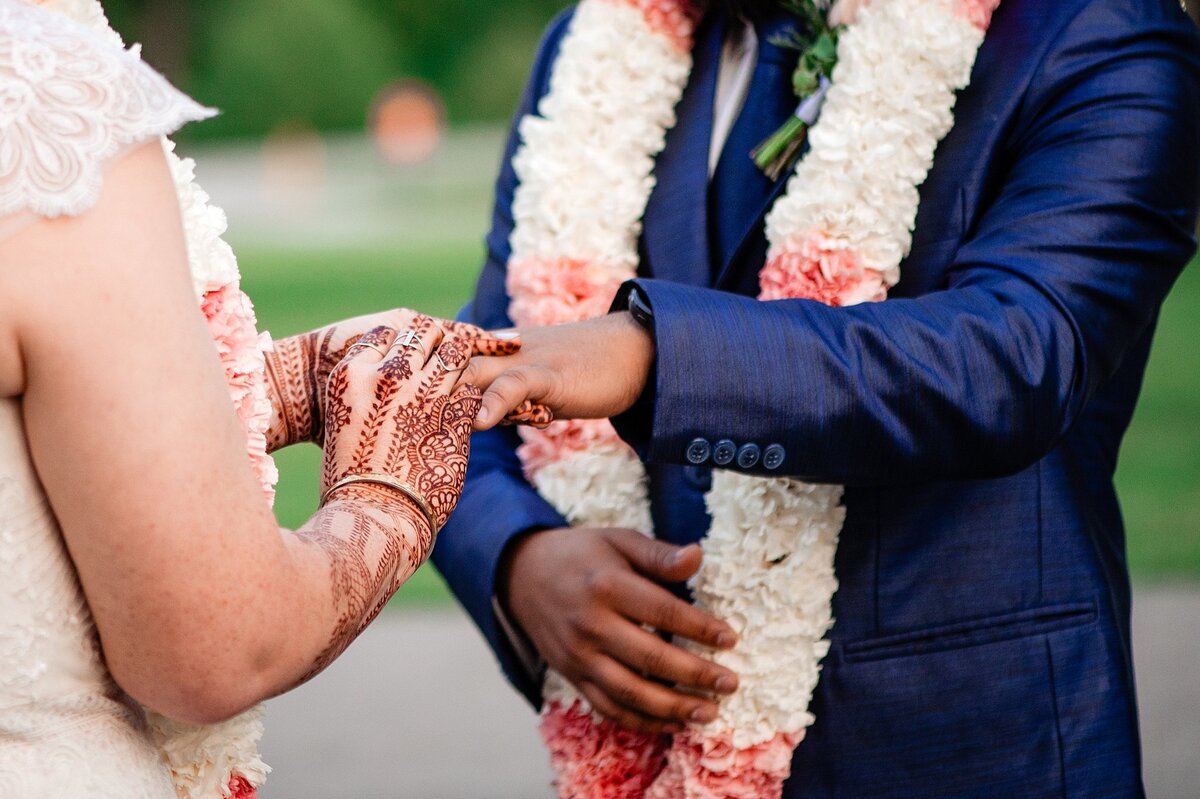 Bride with henna tattoos placing ring on grooms finger