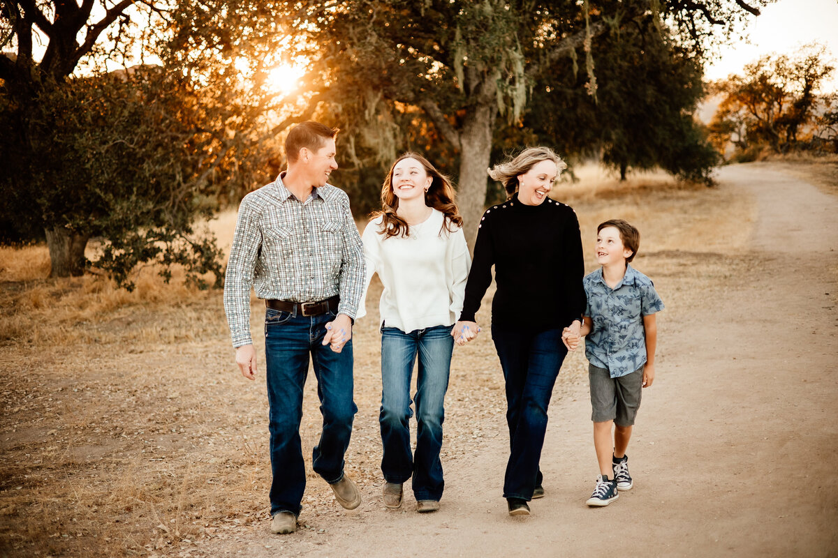 Family of 4 walking at sunset on a backlit path through an oak preserve