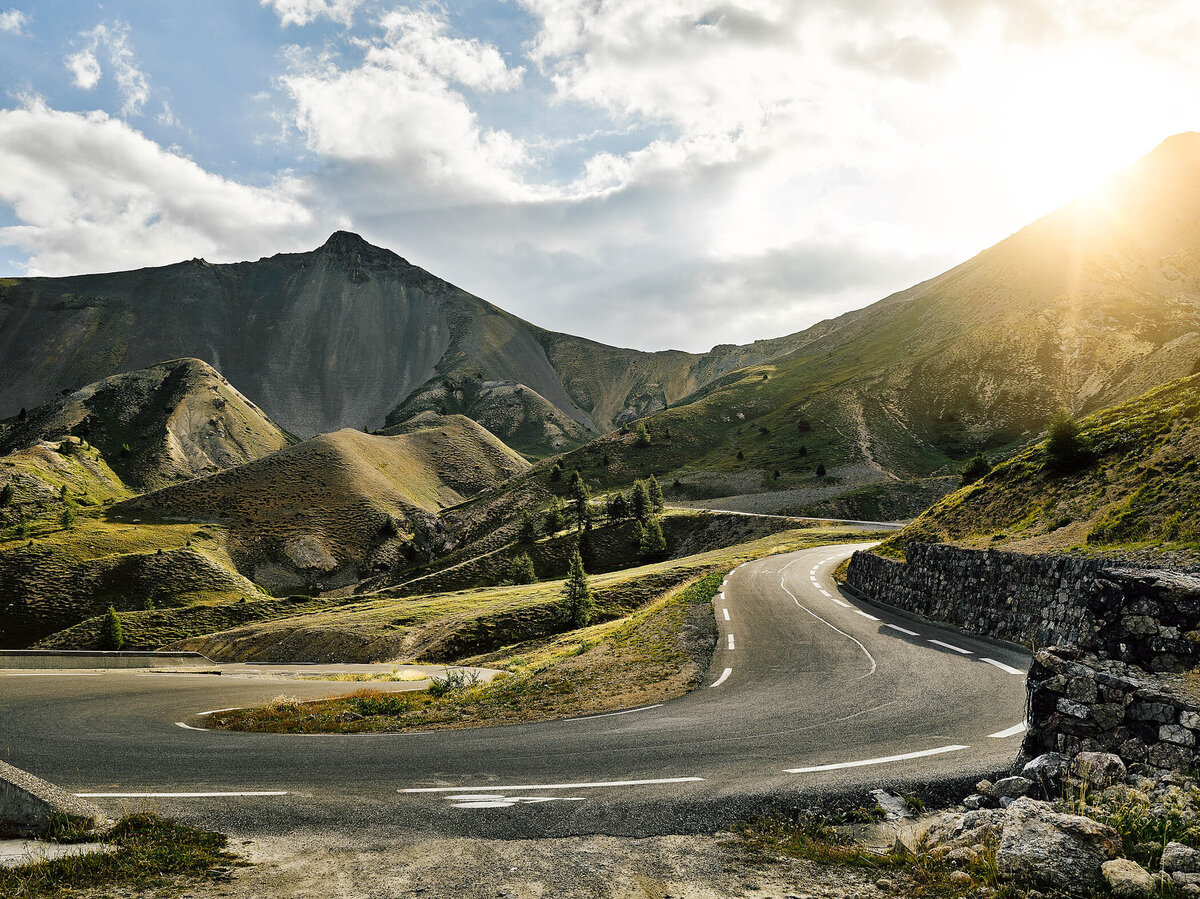 Abendlicht über einer kurvigen Passstraße im Hochgebirge mit markanten Berghängen – professionelle Landschaftsfotografie für Werbung und visuelle Kommunikation