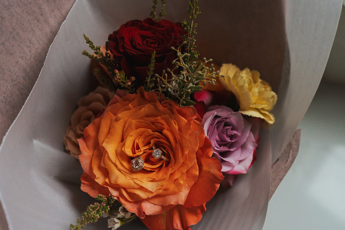 Wedding rings rest atop orange and purple wedding florals 