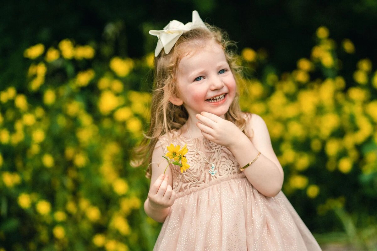 A small girl smiling and holding a flower.