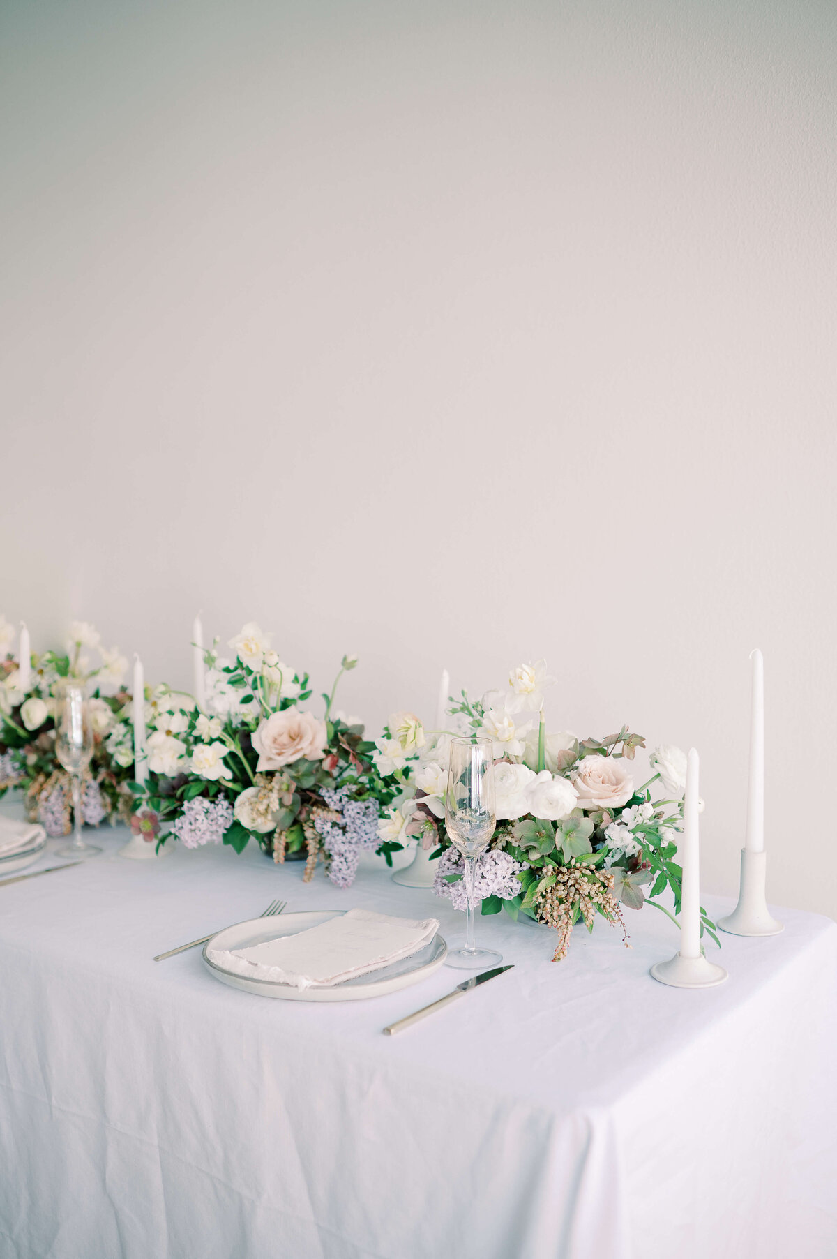 wedding table set up witb white linen, white napkins and floral displays of ivory, blush, designed by wild indigo lavender and greenery