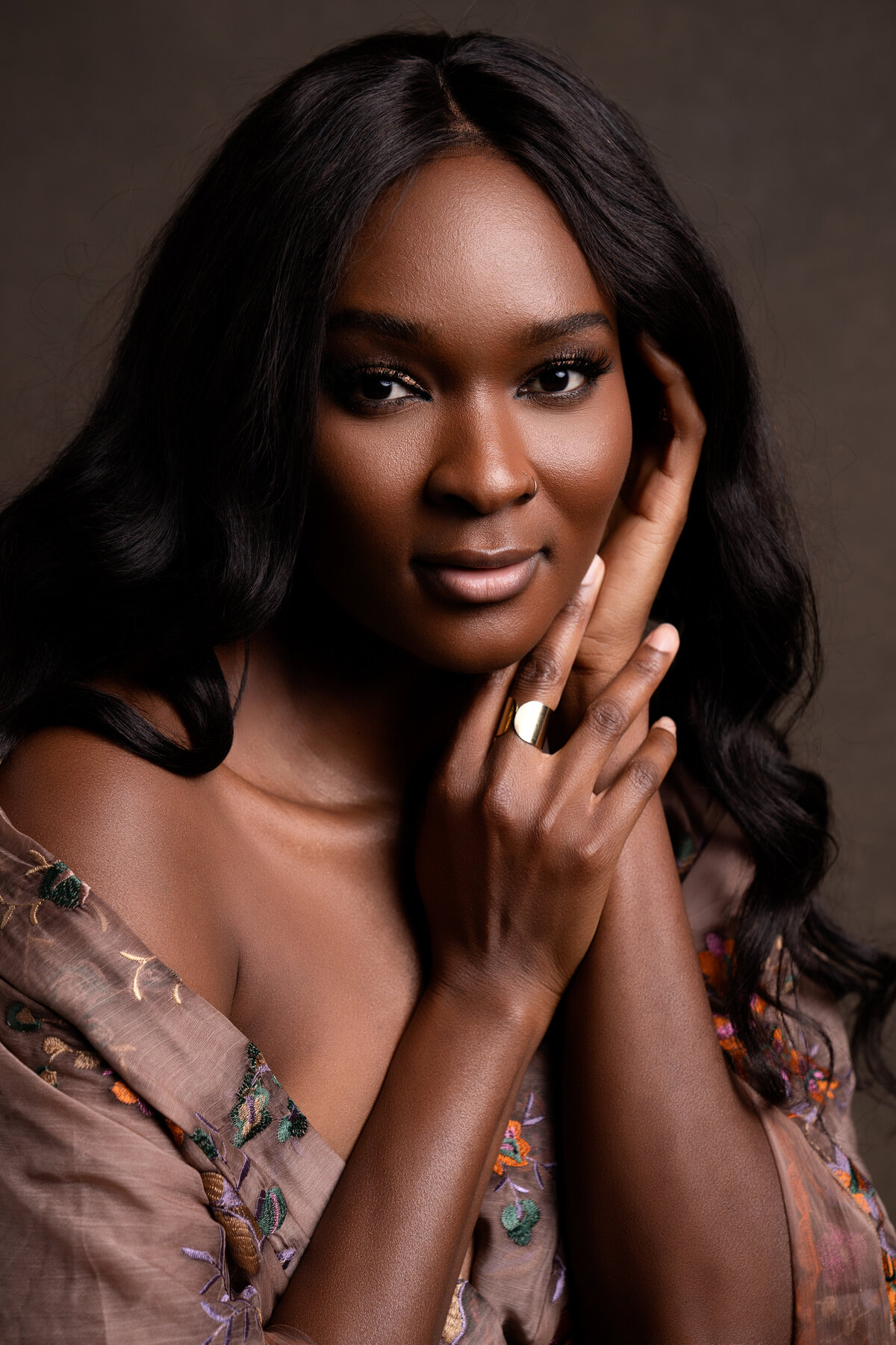 Closeup Portrait of African-American woman with hands near face wearing brown floral dress.