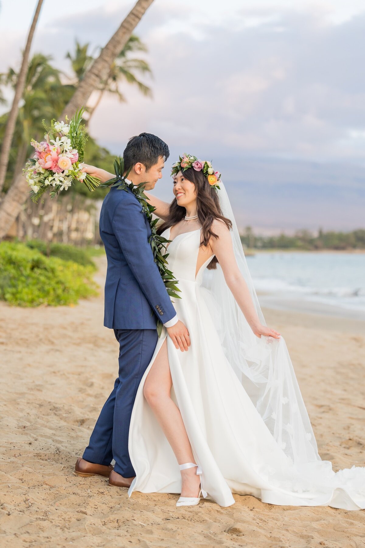 standing in the sand with bride wearing floral crown and groom wearing blue suit