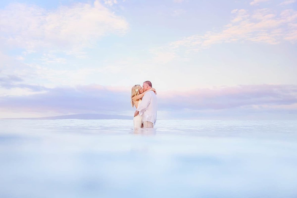 Husband and wife are both wearing white attire while standing in the ocean during their Maui proposal photography session