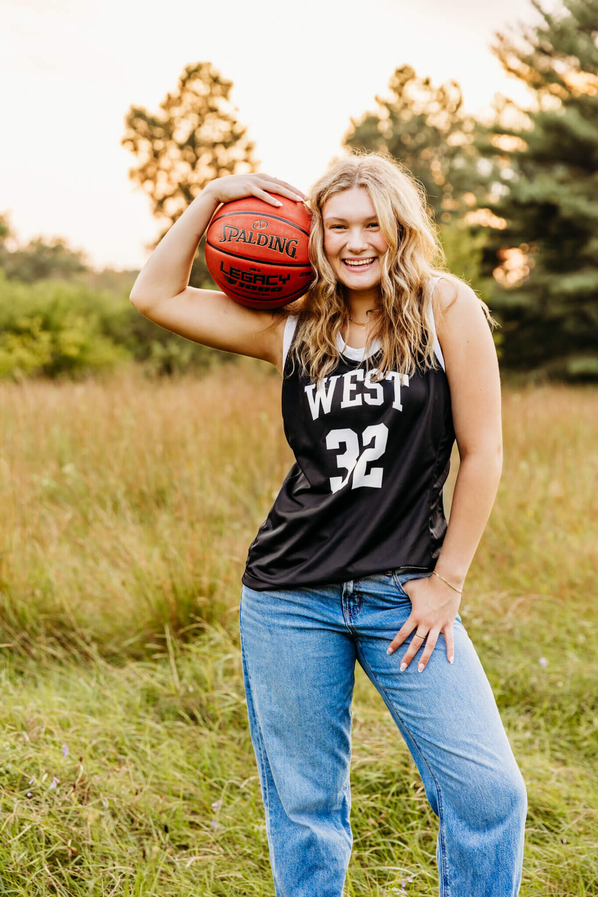 Green Bay high school senior girl wearing a jersey holding a basketball on her shoulder and laughing captured by Ashley Kalbus