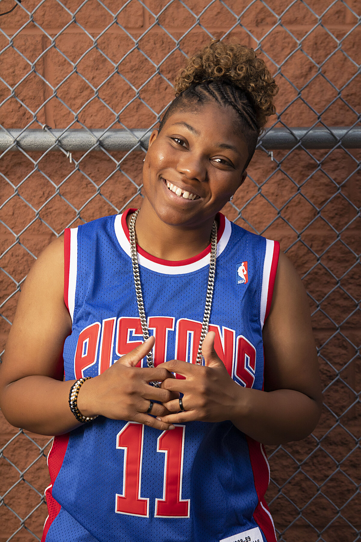 Woman in Detroit Pistons jersey standing in front of a fence