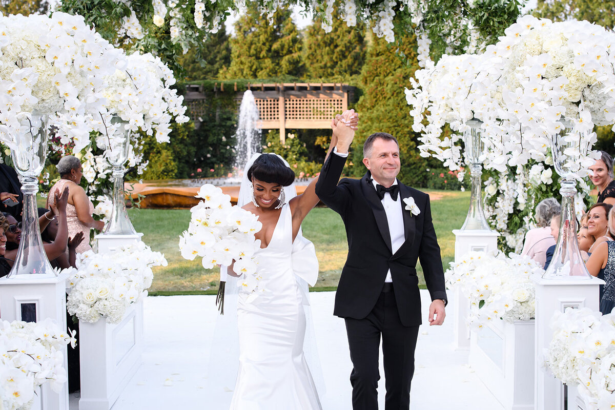 Couple entering their wedding reception under a floral arch.