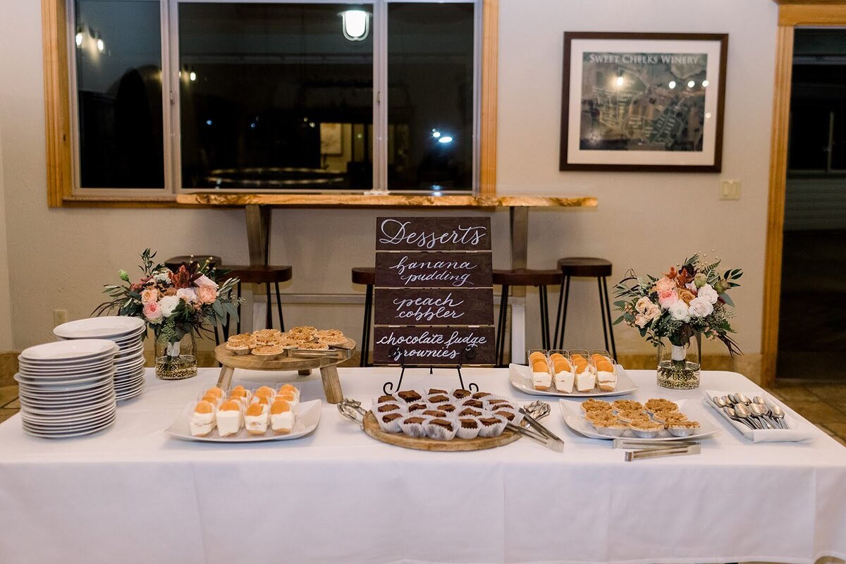 Dessert table at a wedding reception featuring floral arrangements by Flowers and Thyme.