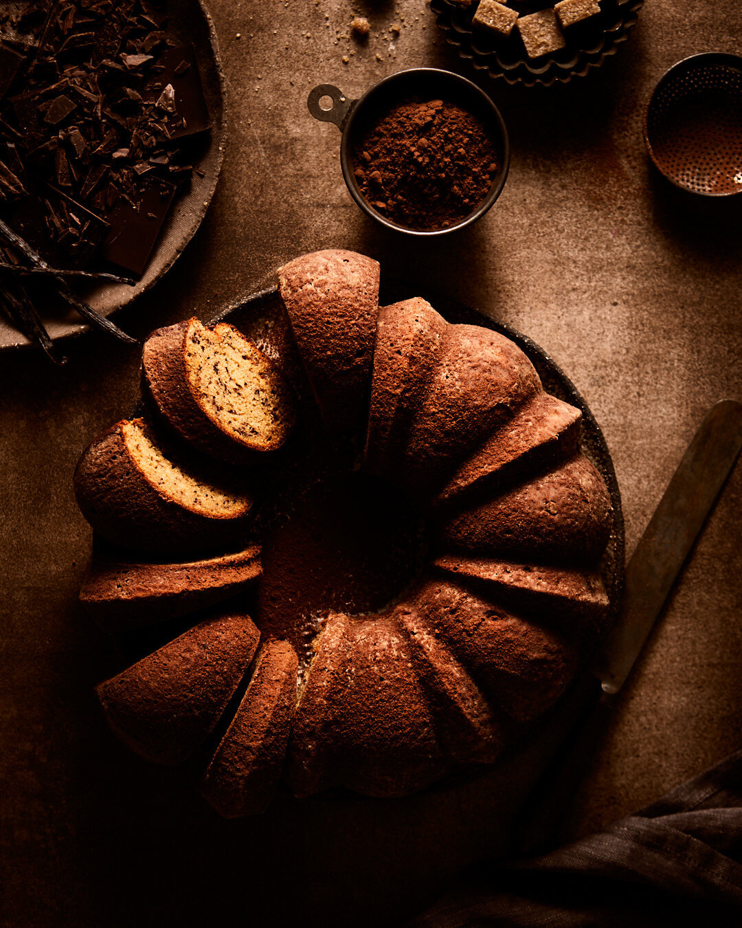 Dark image of a chocolate bundt cake with a few pieces that are sliced.