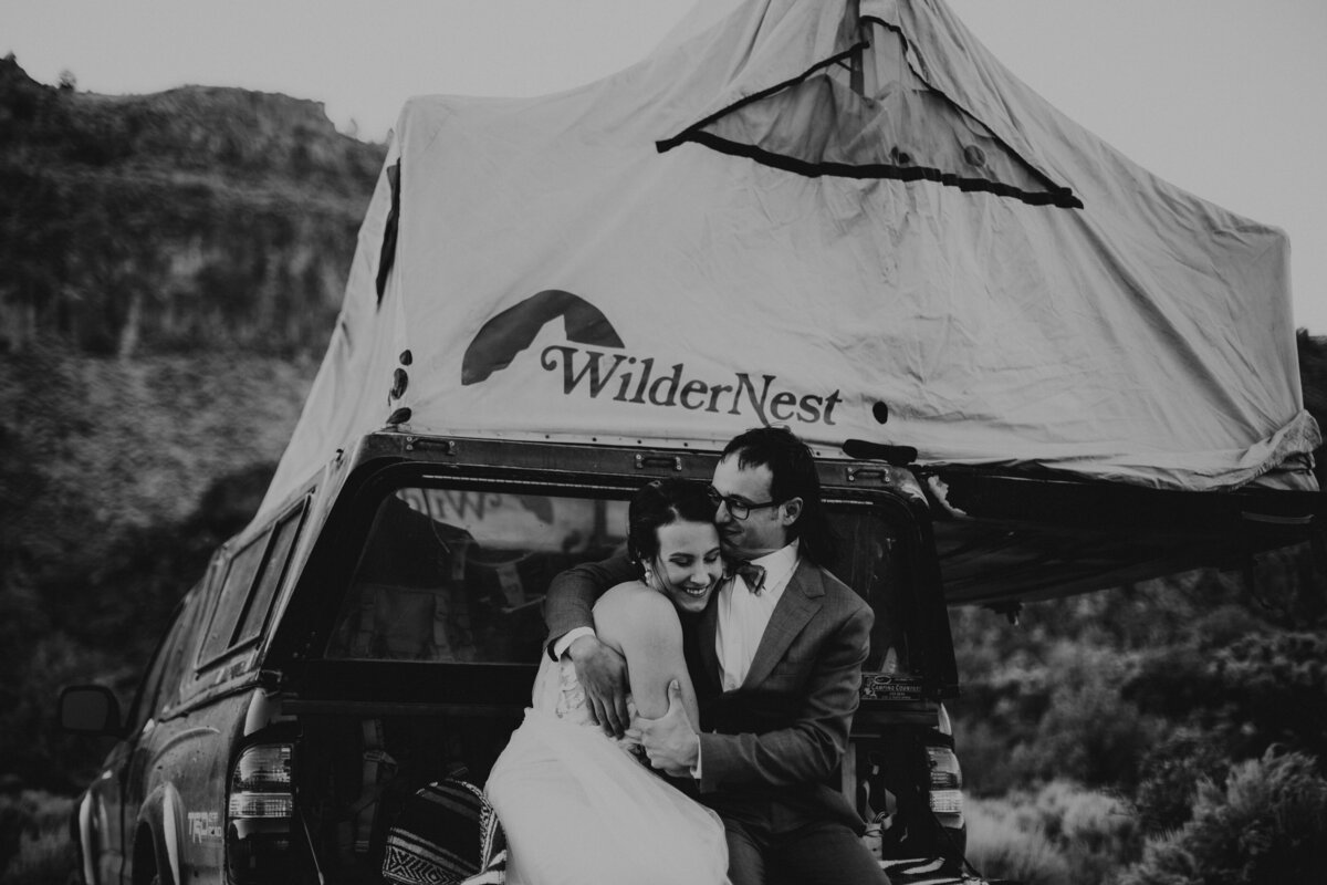 bride and groom sitting on a truck with a tent on top