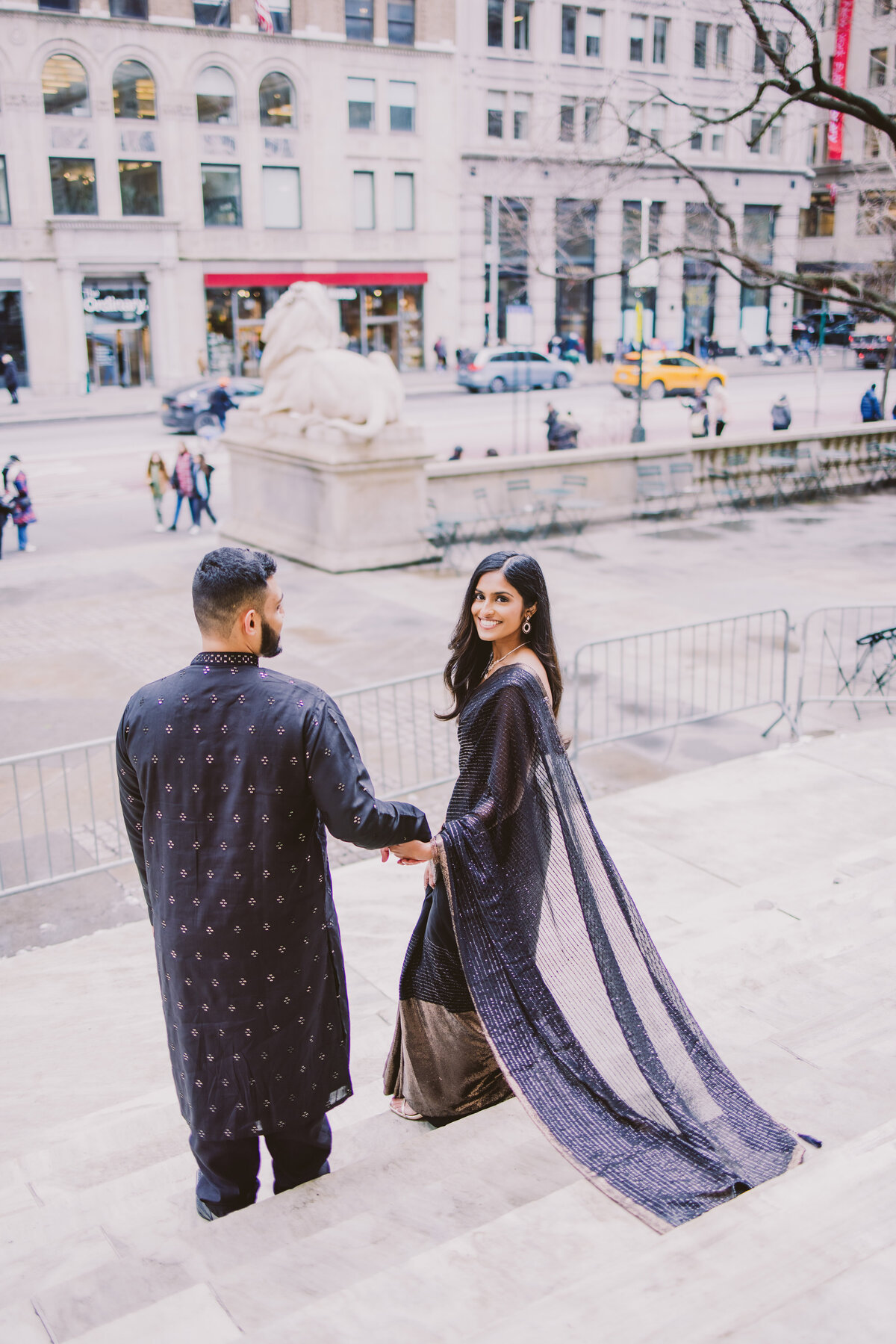 Engaged couple in black indian clothing walk down the steps at the new york public library
