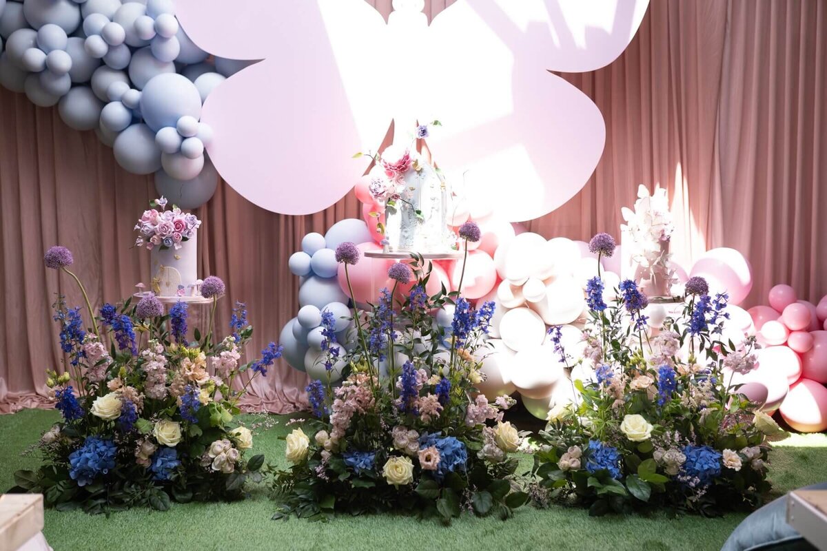 Birthday cakes on tall cake stands covered with garden themed flower decoration and butterfly backdrop