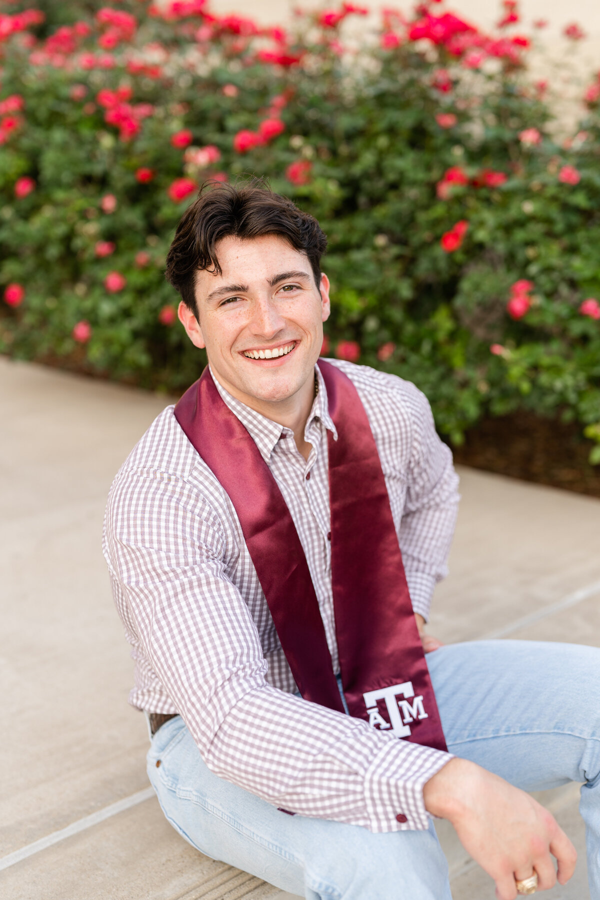 Texas A&M senior guy sitting on stairs and laughing with hand on leg and leaning while wearing maroon stole