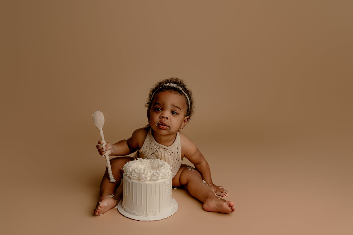 baby eating cake on brown backdrop in phoenix milestone session