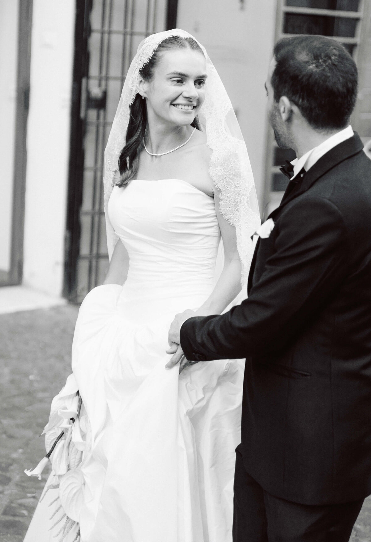 Bride and groom smiling together while walking up steps of historic building

