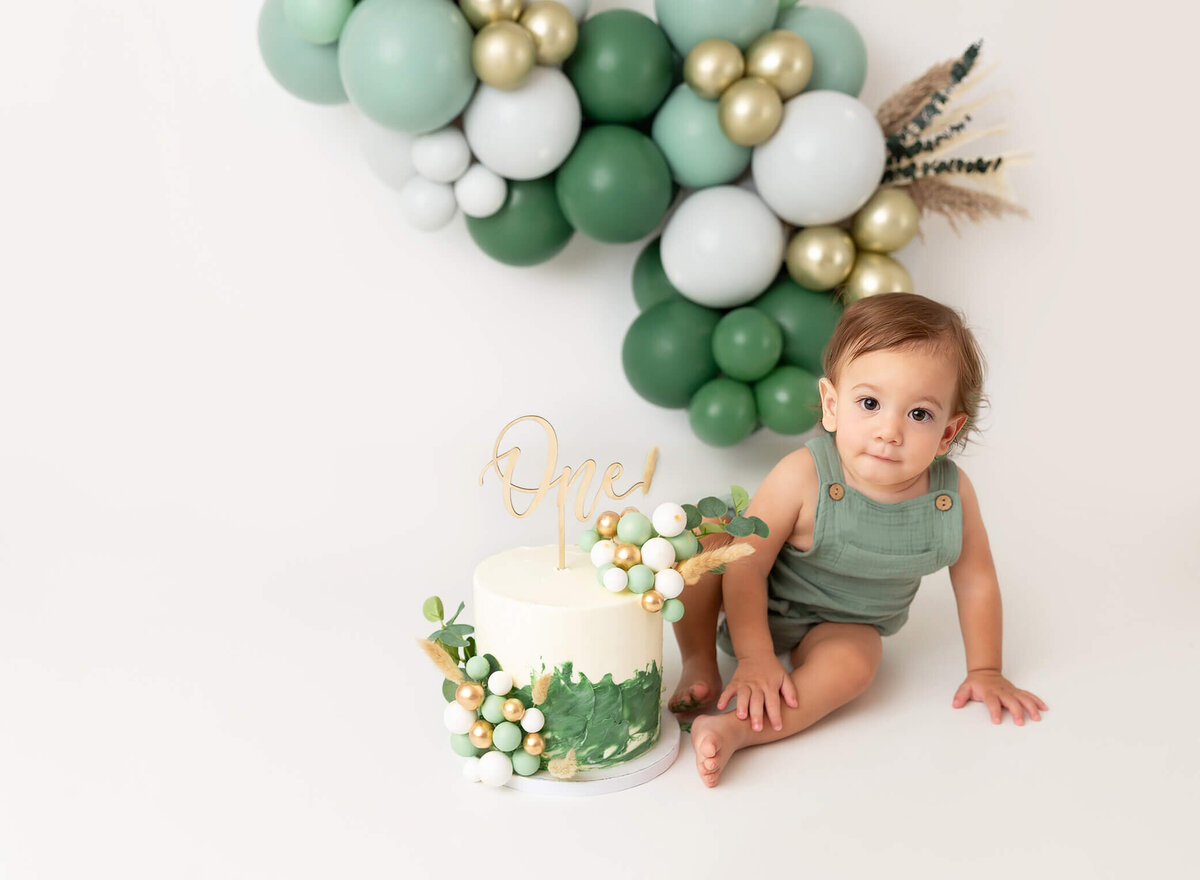 NYC first birthday celebration cake smash pictures with a baby surrounded by a balloon garland and festive cake. A professional photographer in New York City specializing in cake smash sessions