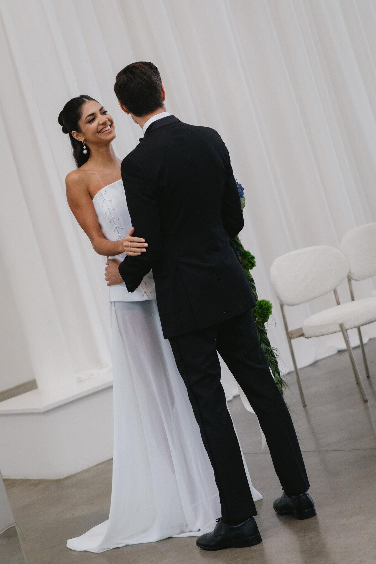 Soft, intimate moment between bride and groom during an editorial wedding photoshoot, framed by greenery inside a modern white NYC studio.