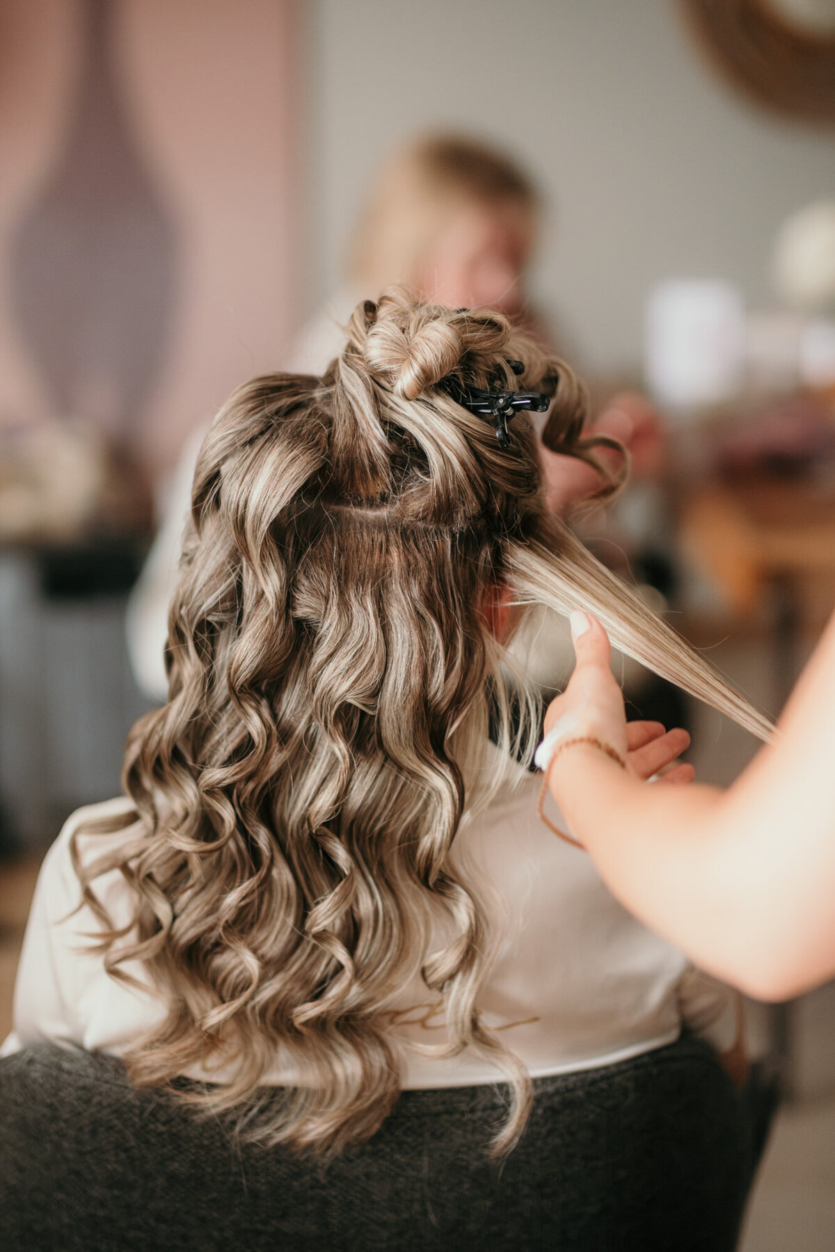 Der Braut werden lockere Wellen in ihre langen blonden Haare gemacht für ihre Brautfrisur.